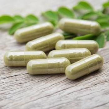 Green pills and small leaves on wooden surface